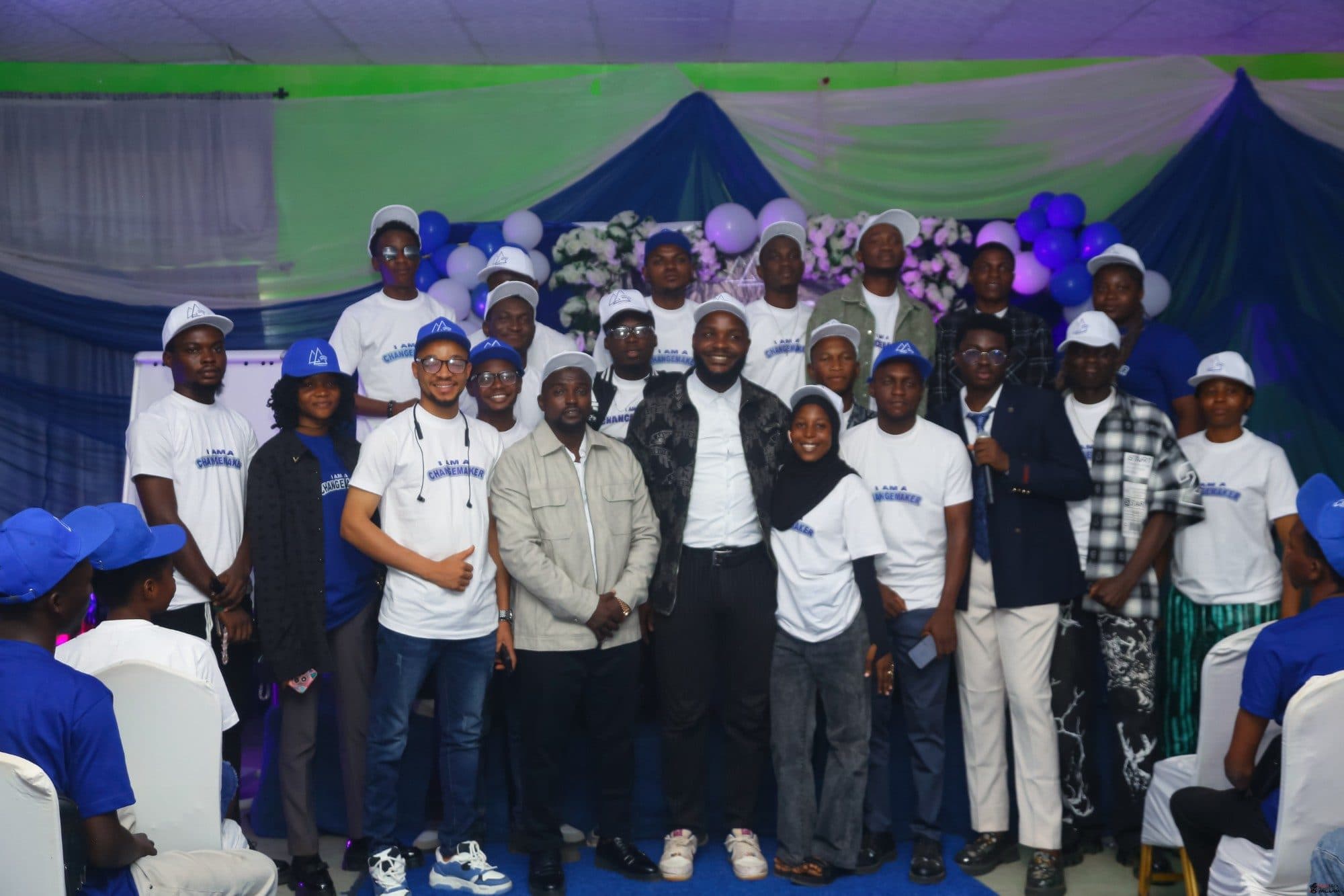 Group photo of members in Changemaker T-shirts and caps posing on stage