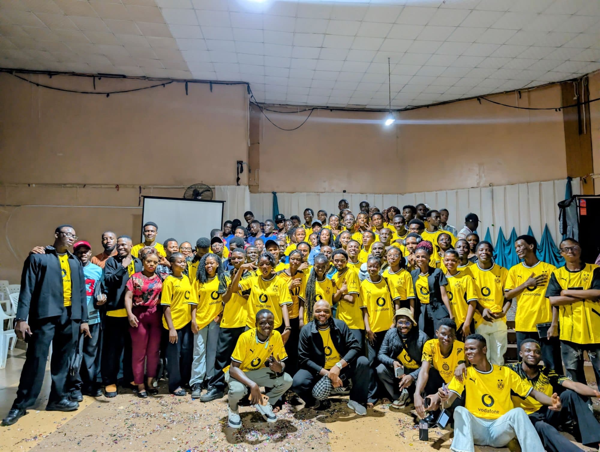 A large group of Accelerator Community members in matching yellow jerseys posing together in a hall